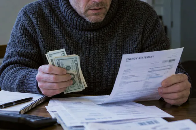 A man in a thick sweater at a desk studying an energy statement with cash in hand